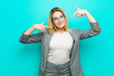 Genç, güzel, sarışın bir kadın kendi gülüşünü işaret ediyor. Olumlu, rahat, düz duvara karşı tatmin olmuş bir tavır takınıyor.