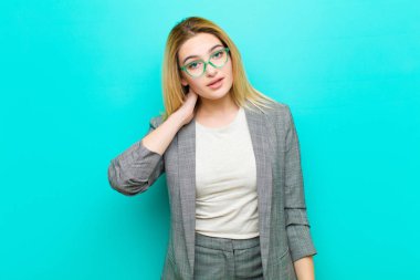 Genç, güzel, sarışın bir kadın neşeli ve kendinden emin bir şekilde gülümsüyor. Sıradan, mutlu, dostça bir gülümsemeyle düz duvara yaslanmış.