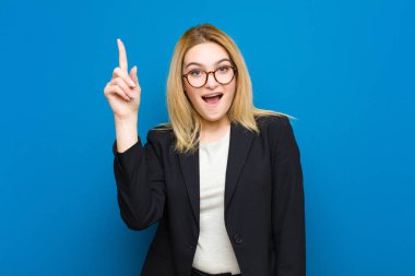 Genç, güzel, sarışın bir kadın hayal kırıklığına uğramış ve hayal kırıklığına uğramış hissediyor. Ciddi görünüyor, sinirlenmiş ve kolları düz duvara dayalı.