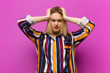 Genç sarışın kadın kendini stresli ve hayal kırıklığına uğramış hissediyor, el ele tutuşuyor, yorgun, mutsuz ve mor duvara karşı migreni var.