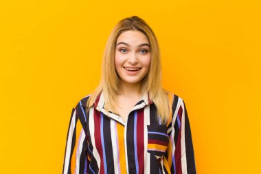 Genç sarışın güzel kadın mutlu ve hoş bir şekilde şaşırmış görünüyor, turuncu duvarın karşısında büyüleyici ve şok olmuş bir ifadeyle heyecanlanıyor.