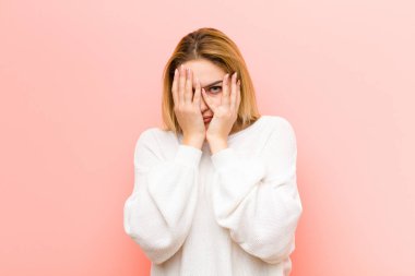 Genç, güzel, sarışın bir kadın korkmuş ya da utanmış hissediyor. Gözleri yarı kapalı pembe düz duvara bakıyor ya da dikizliyor.