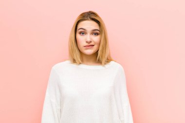 Genç, güzel sarışın kadın şaşkın ve şaşkın görünüyor, gergin bir hareketle dudaklarını ısırıyor, pembe düz duvara karşı sorunun cevabını bilmiyor.