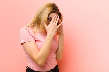 Genç, güzel, sarışın bir kadın üzgün, hayal kırıklığına uğramış bakışlarıyla gözlerini kapıyor. Ağlıyor, pembe düz duvara yan bakıyor.