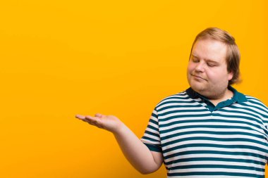 Genç, iri yarı, mutlu ve güler yüzlü bir adam. Elinde turuncu duvara karşı duran bir nesneye ya da konsepte bakıyor.