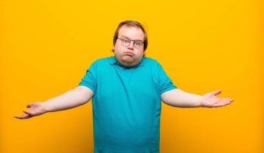 Genç büyük adam şaşkın ve şaşkın hissediyor, doğru cevap ya da karardan emin değil, turuncu duvara karşı bir seçim yapmaya çalışıyor.