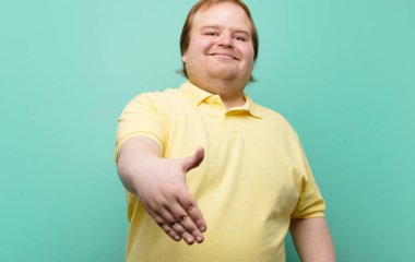 Genç büyük adam gülümsüyor, seni selamlıyor ve başarılı bir anlaşma için el sıkışmayı teklif ediyor, mavi duvara karşı işbirliği konsepti.