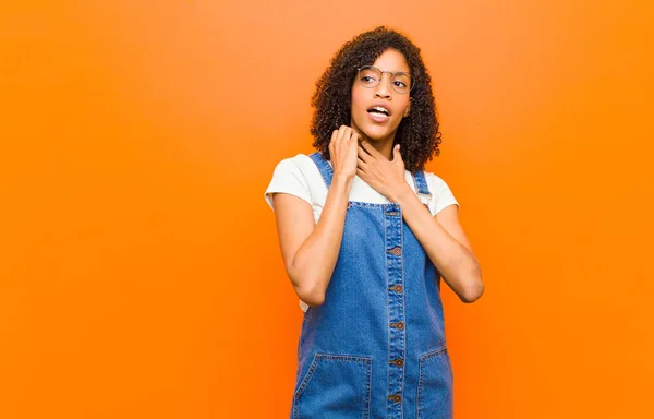 young pretty black woman feeling stressed, frustrated and tired, rubbing painful neck, with a worried, troubled look against orange wall