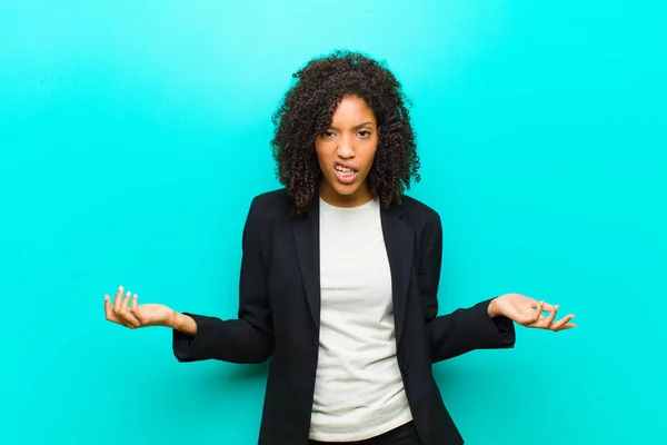 young black woman looking shocked, angry, annoyed or disappointed, open mouthed and furious against blue wall