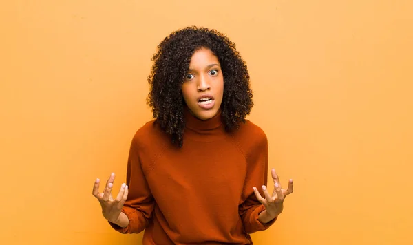 young pretty black woman looking angry, annoyed and frustrated screaming wtf or whats wrong with you against orange wall