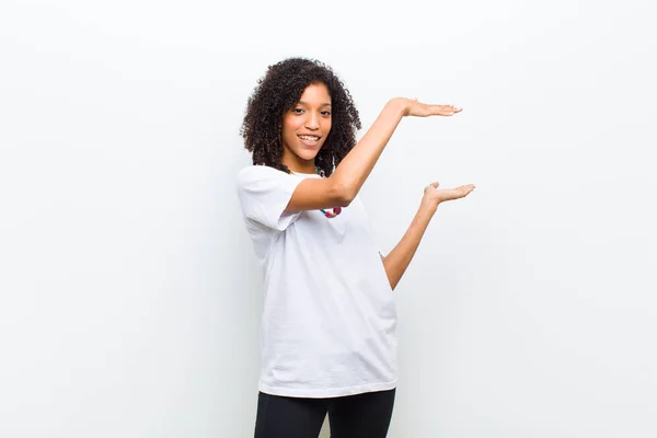 young cool african american woman smiling, feeling happy, positive and satisfied, holding or showing object or concept on copy space