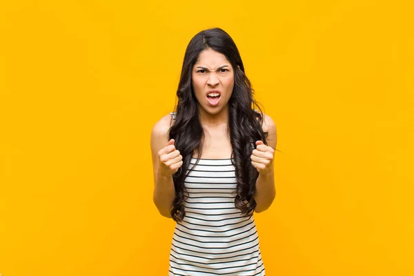 オレンジ色の壁に激怒した若いラテン系の女性がいらいらし いらいらし 怒っている表情とタイトな拳で積極的に叫んでいる — ストック写真