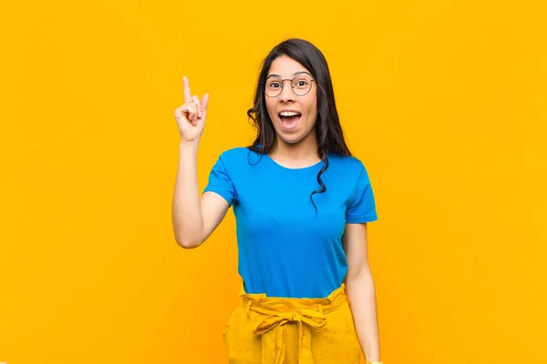 年轻漂亮的拉丁女人在意识到一个想法后 高兴地举起手指 尤里卡 觉得自己是个快乐而兴奋的天才 相对于橙色墙 — 图库照片