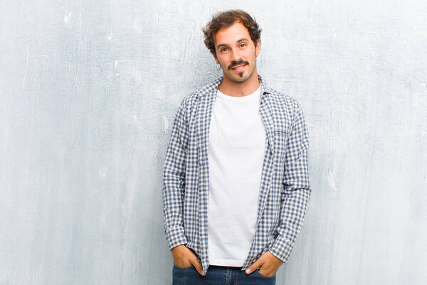 молодой красивый мужчина улыбается весело и небрежно с положительным, счастливым, уверенным и расслабленным выражением, изолированным от плоской стены
