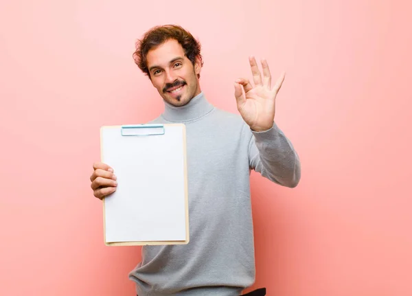 young handsome man with a sheet of paper against pink flat wall