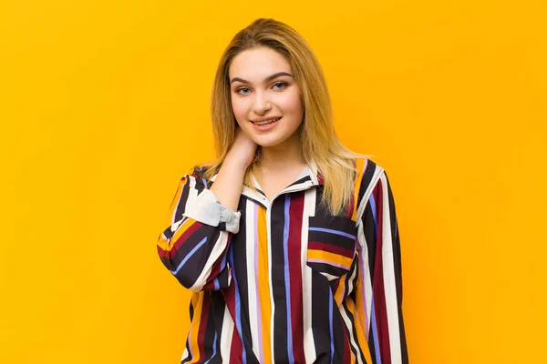 オレンジ色の壁に対して明るく自信を持って笑う若いブロンドの可愛い女性 — ストック写真