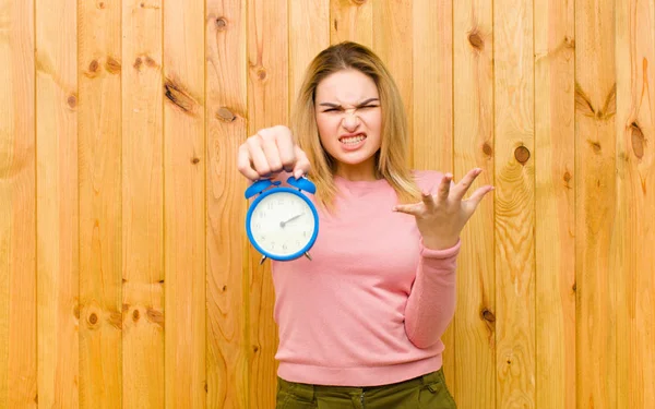 木製の壁に目覚まし時計を持つ若いかなりブロンドの女性 — ストック写真