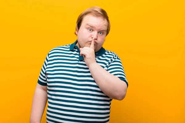 young big size man asking for silence and quiet, gesturing with finger in front of mouth, saying shh or keeping a secret against orange wall