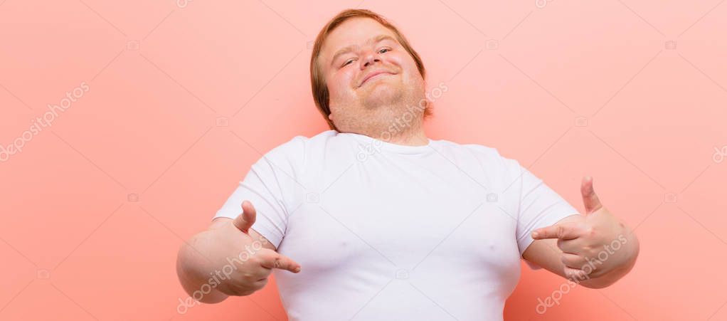 young big size man looking proud, arrogant, happy, surprised and satisfied, pointing to self, feeling like a winner against pink wall
