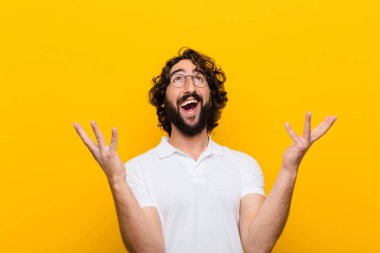 Genç çılgın adam kendini mutlu, şaşkın, şanslı ve şaşırmış hissediyor. Zaferi kutluyor. İki eli de havada, sarı duvara karşı.