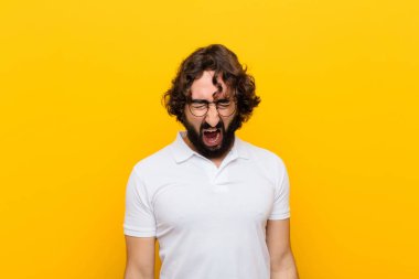 Genç çılgın adam agresif bir şekilde bağırıyor, sinirli, sinirli, öfkeli ya da sinirli görünüyor, sarı duvara karşı hayır diye bağırıyor.