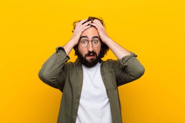 Dehşete kapılmış ve şok olmuş hisseden genç bir adam, sarı duvara karşı ellerini kaldırıyor ve panikliyor.