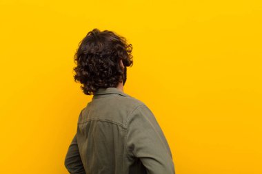 Genç çılgın adam şaşırmış ya da dolu hissediyor ya da şüphe ve sorular, merak ediyor, elleri kalçasında, sarı duvara bakan dikiz aynası