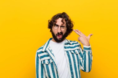 Genç çılgın adam mutsuz ve stresli görünüyor, intihar jesti elle silah işareti yapıyor, kafasını sarı duvara dayıyor.