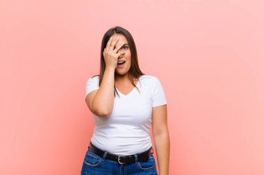 Genç, güzel, İspanyol bir kadın mutlu, heyecanlı ve pozitif hissediyor. Elleri ağızda, pembe duvara karşı bağırıyor.