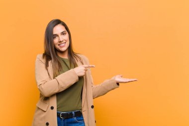 Genç, güzel bir kadın gülümsüyor, mutlu, kaygısız ve tatmin olmuş hissediyor. Fotokopi alanındaki konsepte ya da fikre işaret ediyor. Turuncu duvara yaslanmış.