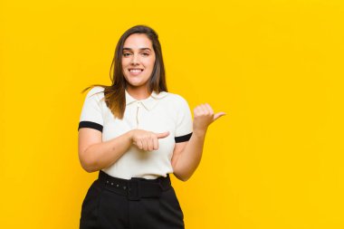 Genç, güzel bir kadın neşeli ve tesadüfen fotokopi alanını işaret ederek turuncu duvara yaslanmış mutlu ve tatmin olmuş hissediyor.