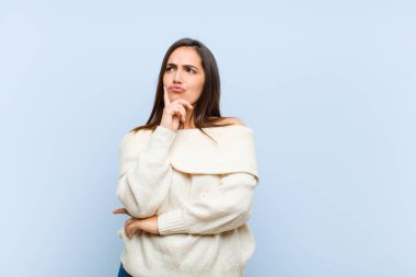 Genç, güzel bir kadın düşünüyor, kuşkulu ve şaşkın hissediyor, farklı seçenekleri var, mavi arka plana karşı hangi kararı vereceğini merak ediyor.