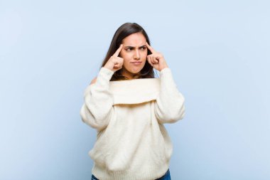 Genç ve güzel bir kadın konsantre olmuş ve bir fikir üzerinde kafa yoruyor, mavi arka plandaki bir soruna bir çözüm hayal ediyor.