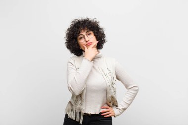 Genç, güzel afro kadın ciddi, düşünceli ve güvensiz görünüyor, bir kolu çapraz ve çene üzerinde, seçenekleri tartıyor