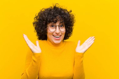 Genç, güzel afro kadın mutlu ve heyecanlı görünüyor. Beklenmedik bir sürprizle şoke oldu. İki eli de açık.