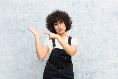 Genç, güzel afro kadın neşeyle gülümsüyor ve yan taraftaki fotokopi alanını işaret ediyor, bir nesneyi gösteriyor ya da reklamını yapıyor.
