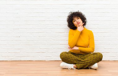Genç, güzel afro kadın ciddi, düşünceli ve güvensiz görünüyor, bir kolu çapraz ve çene üzerinde, seçenekleri tartıyor yerde oturuyor