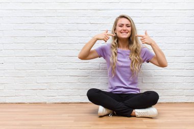 Genç, sarışın, güzel bir kadın. Kendine güvenerek gülümsüyor. Geniş bir gülümseme, pozitif, rahat, tatmin olmuş bir tavır.