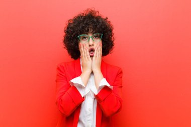 Genç, güzel afro kadın şok olmuş ve korkmuş hissediyor, ağzı açık ve elleri yanaklarında korkmuş görünüyor.