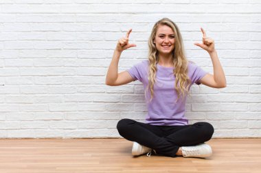 Genç, sarışın, güzel bir kadın kendi gülüşünü çiziyor, iki eliyle, pozitif ve mutlu görünüyor, sağIık kavramı