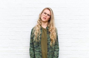 Genç sarışın kadın şaşkın ve şaşkın hissediyor, aptal, afallamış bir ifadeyle tuğla duvar arkasında beklenmedik bir şeye bakıyor.