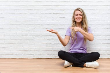 Genç sarışın güzel kadın neşeyle gülümsüyor ve bir objeyi gösteren ya da reklamını yapan avuç içindeki fotokopi alanını işaret ediyor.