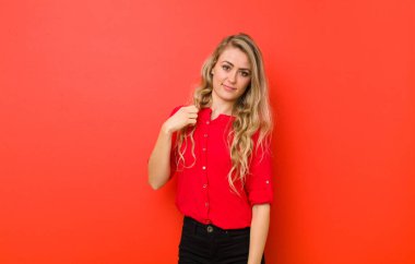 Genç sarışın kadın küstah, başarılı, pozitif ve gururlu görünüyor, kırmızı duvara karşı kendini işaret ediyor.