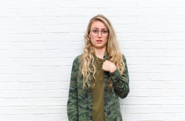 Genç sarışın kadın şaşkın, şaşkın ve güvensiz hissediyor. Kendini gösterip kim olduğumu soruyor. Ben mi? tuğla duvar arkaplanı