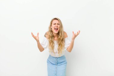 Genç sarışın kadın öfkeyle bağırıyor, strese giriyor ve elleri havada neden beyaz duvara yaslandığımı söylüyor.