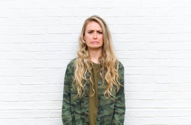 Genç sarışın kadın üzgün ve mızmız, mutsuz bir bakışla ağlıyordu. Olumsuz ve hayal kırıklığına uğramış bir tavırla tuğla duvar arkasında ağlıyordu.