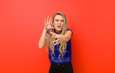 Genç sarışın kadın korkmuş, korku ve panik içinde geri çekiliyor, kırmızı duvara karşı bir kabusa tepki veriyor.