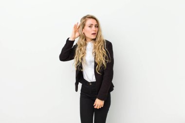 Genç sarışın kadın gülümsüyor, tuhaf bir şekilde yan tarafa bakıyor, dedikoduları dinlemeye çalışıyor ya da beyaz duvara karşı bir sırrı duymaya çalışıyor.