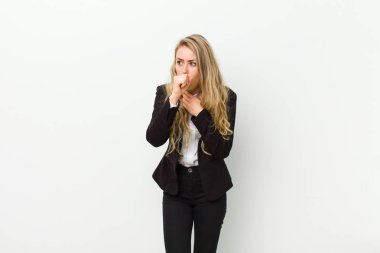 Genç sarışın kadın boğaz ağrısı ve grip belirtileri gösteriyor. Ağzı beyaz duvara yapışmış öksürüyor.