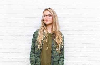 Genç sarışın kadın merak ediyor, mutlu düşünceler ve fikirler düşünüyor, hayal kuruyor, duvarın arkasında yer arıyor.